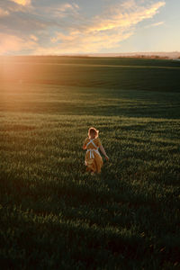 Young female in vintage rustic style dress running alone in vast green grassy field in summer evening in countryside