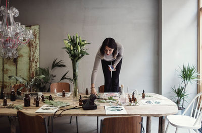 Young woman standing on chair arranging table at perfume workshop