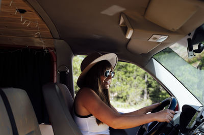 Side view of female traveler sitting on driver seat in van and enjoying road trip in summer