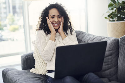 Smiling young woman using phone while sitting on sofa at home