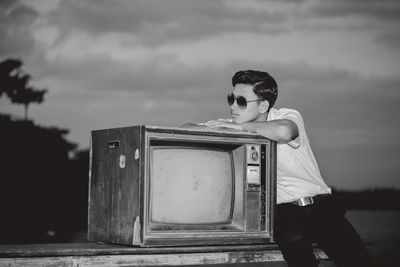 Side view of smiling teenage boy sitting by television set against sky