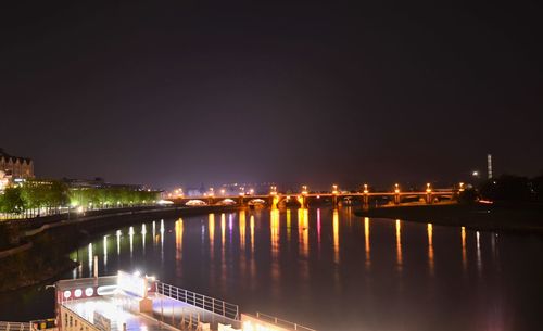 Illuminated buildings by river against sky at night