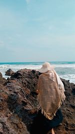 Rear view of woman walking on rock at beach against sky