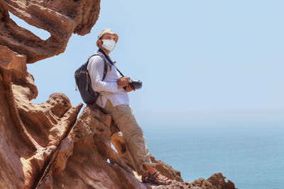 Man standing on rock by sea against clear sky