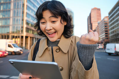 Portrait of young woman using digital tablet while standing in city