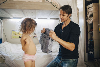 Father dressing daughter in bedroom