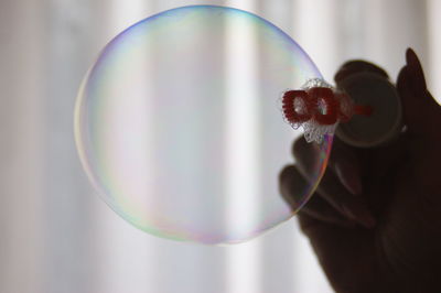 Cropped image of woman holding bubble wand against curtain