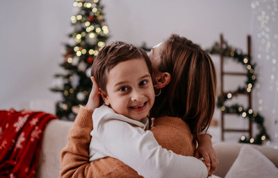 Mother keeps in arms, tender embrace, gently hugs child kid son boy in christmas background