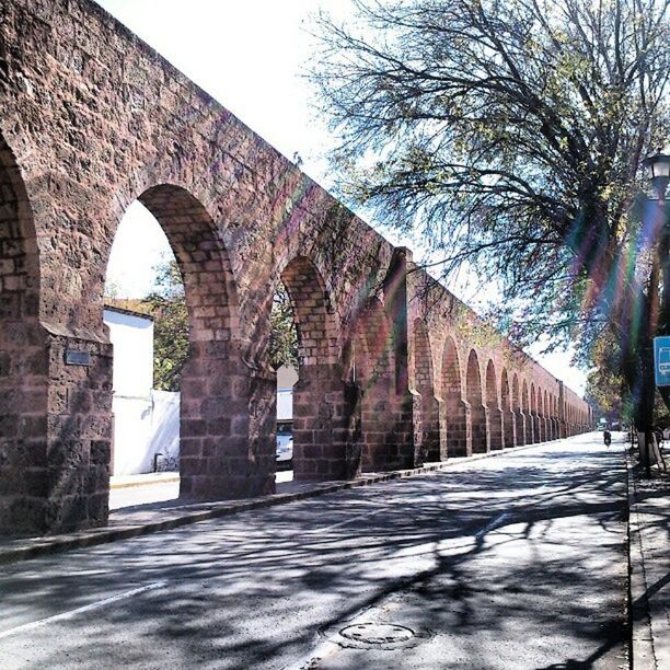 architecture, built structure, building exterior, the way forward, arch, street, building, diminishing perspective, cobblestone, history, day, old, wall - building feature, outdoors, sunlight, road, tree, footpath, no people, city