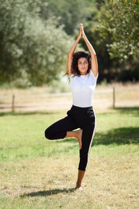 Full length of young woman practicing yoga in tree pose at park