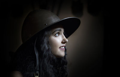 Close-up of teenage girl wearing hat while looking away over black background