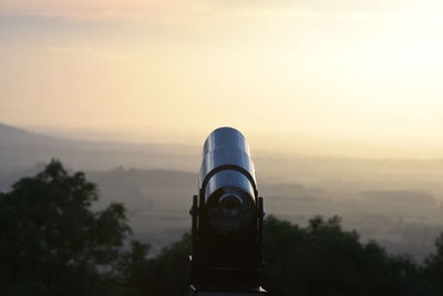 Close-up of coin-operated binoculars against sky during sunset