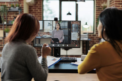 Rear view of businesswomen talking on video call office