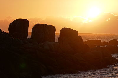 Rock formations at beach against sky during sunset