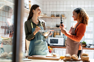 Smiling woman vlogging while her friend preparing food in kitchen