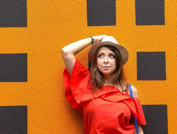 Beautiful woman holding hat while leaning on wall