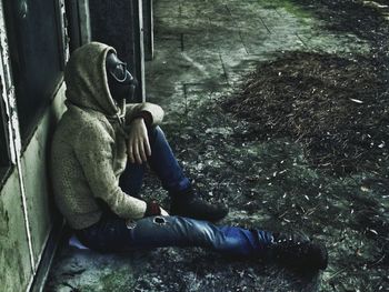 High angle view of man wearing gas mask while sitting outside old building