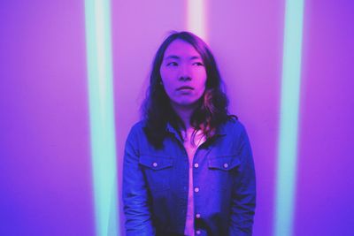 Portrait of beautiful young woman standing against purple wall