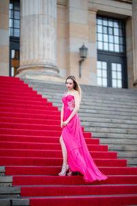 Female model wearing pink evening gown while standing on steps