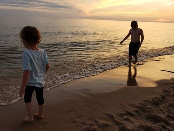 Siblings standing at beach during sunset