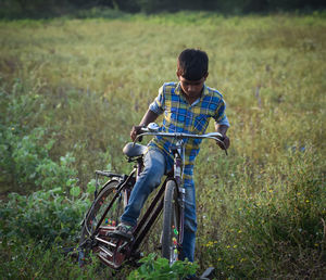 Rear view of boy with bicycle on field