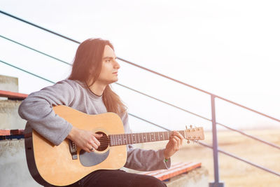 Young woman playing guitar against sky