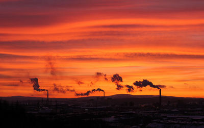 Smoke emitting from factory against orange sky