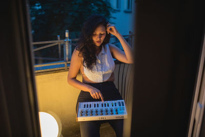 High angle view of young woman playing piano while sitting on balcony seen through doorway