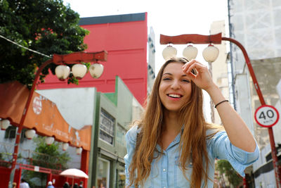 Portrait of smiling young woman against buildings in city