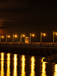 Illuminated bridge over river against sky at night