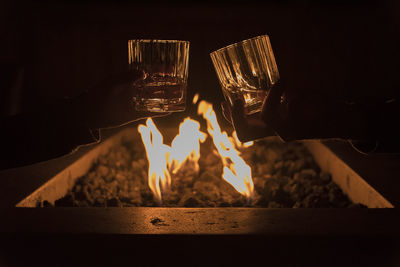 Cropped hands of couple toasting scotch whiskey glasses by bonfire