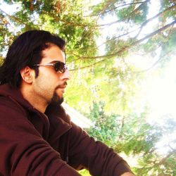 Portrait of young man looking away against trees