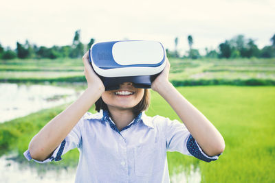 Girl smiling while wearing virtual reality simulator on grassy field against sky