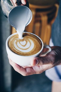 Cropped hands pouring milk in cappuccino