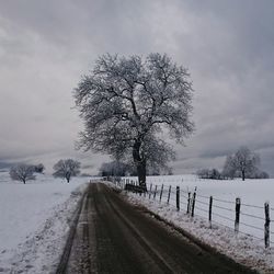 Road passing through field against cloudy sky