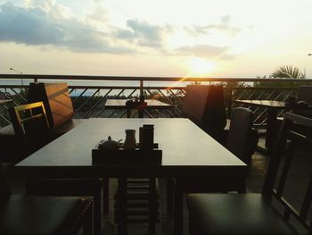 Empty chairs and tables at restaurant against sky during sunset