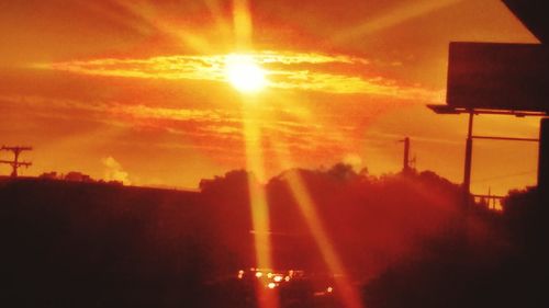 Low angle view of sun streaming through clouds during sunset