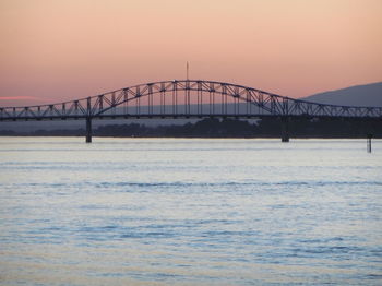 Bridge over sea against orange sky