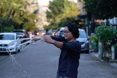 Young man splashing water while standing on road in city