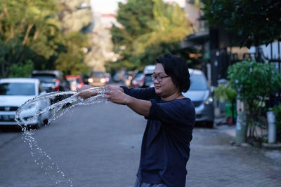 Side view of man standing splashing water on street