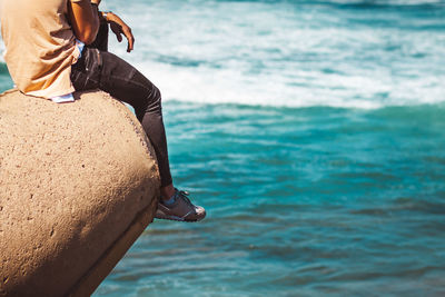 Low section of man sitting on rock over sea