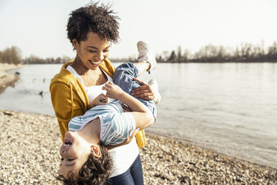 Playful mother carrying son while playing by lake