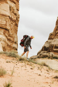 Hiker in camouflage and big backpack walks in sand in utah