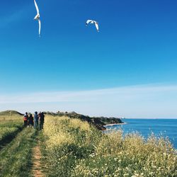 People walking on cliff by sea against sky