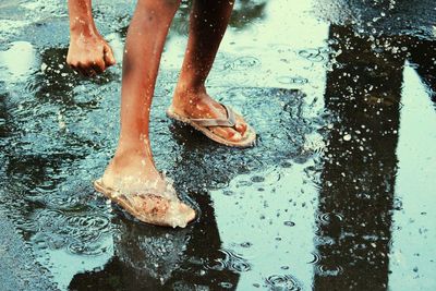 Low section of person standing on wet road during rainy season