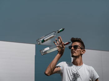 Young man playing with bottles against sky