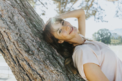 Portrait of young woman against tree trunk
