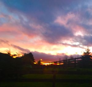 Silhouette of trees on field against dramatic sky