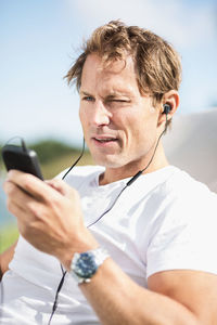 Mature man wearing headphones while using smart phone outdoors