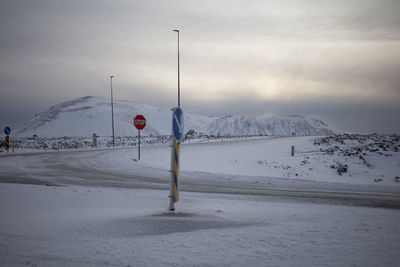 Road sign on snow covered land against sky